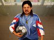 Ein Sportlehrer mit langen Haaren blickt mit Ball unter dem Arm in die Kamera