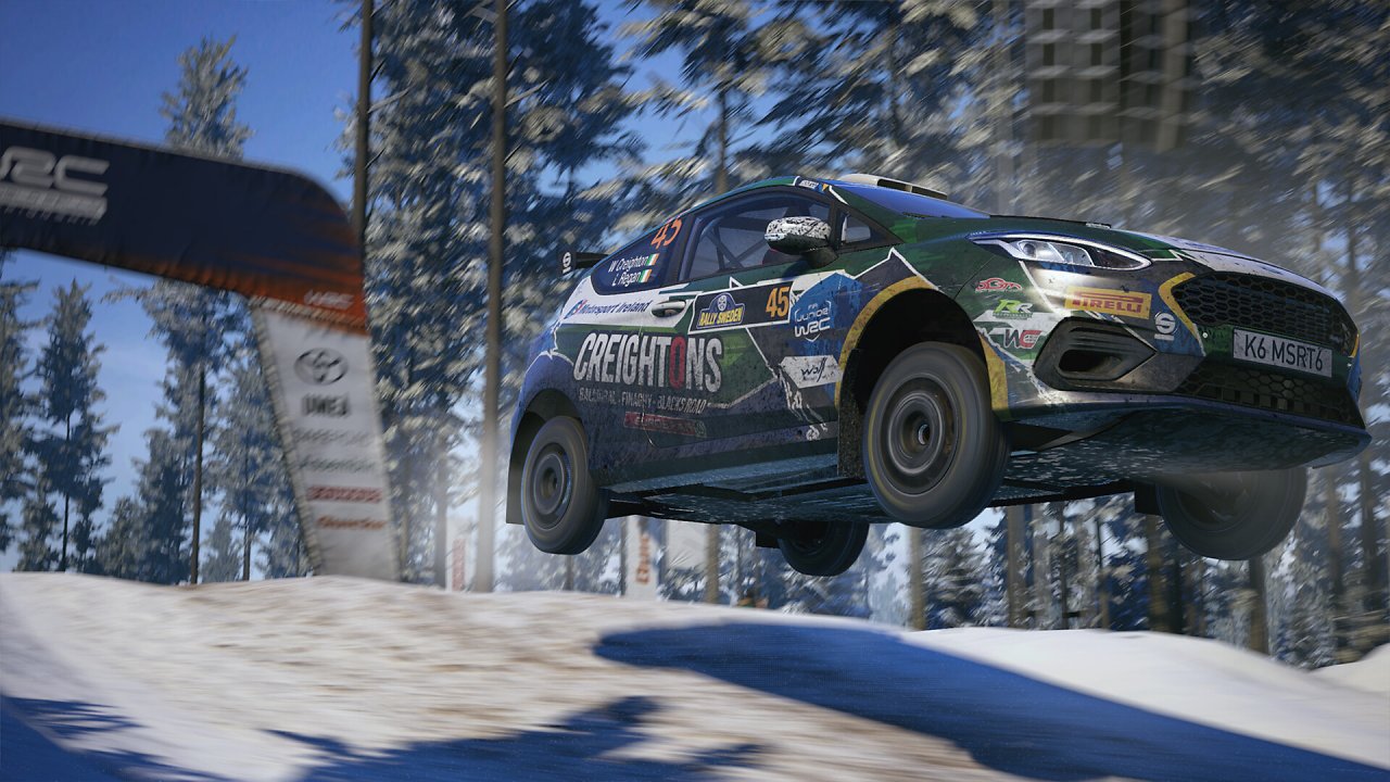Ein Rennauto springt über eine verschneite Kuppe.