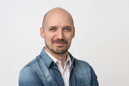 Weißer Mann in seinen Dreißigern mit Glatz, der direkt in die Kamera schaut
